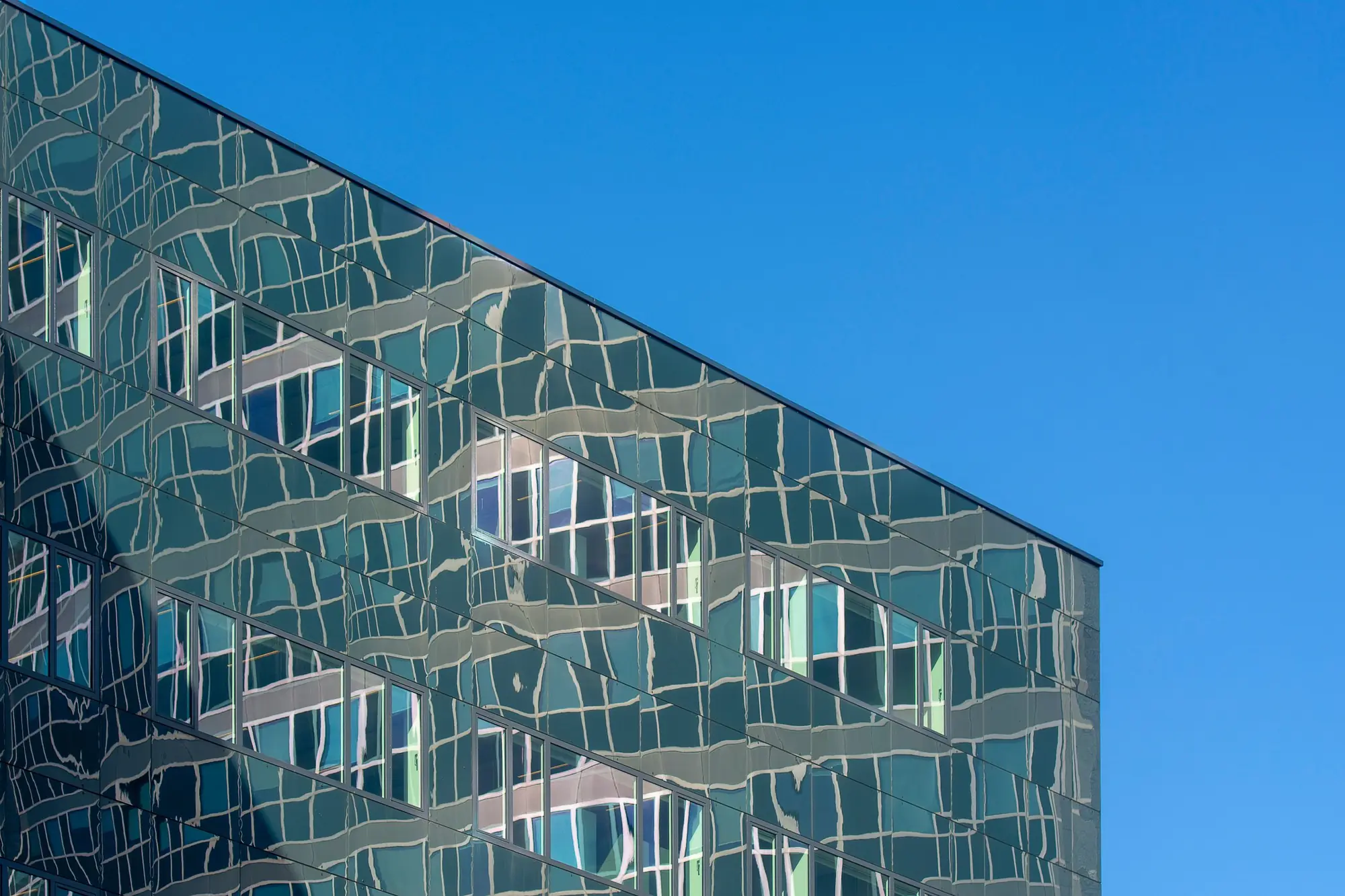 A glass office facade at an angle, its panels reflecting a clear sky.
