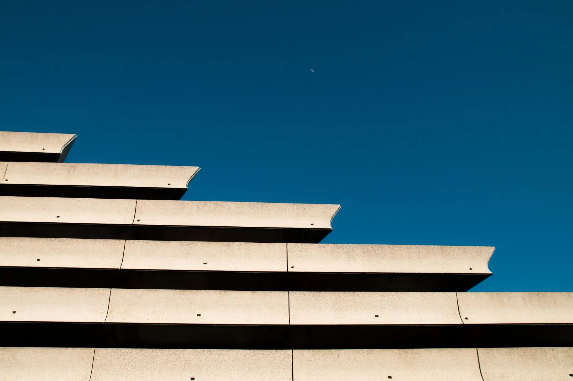 A concrete building rising in stacked horizontal tiers against a clear sky.