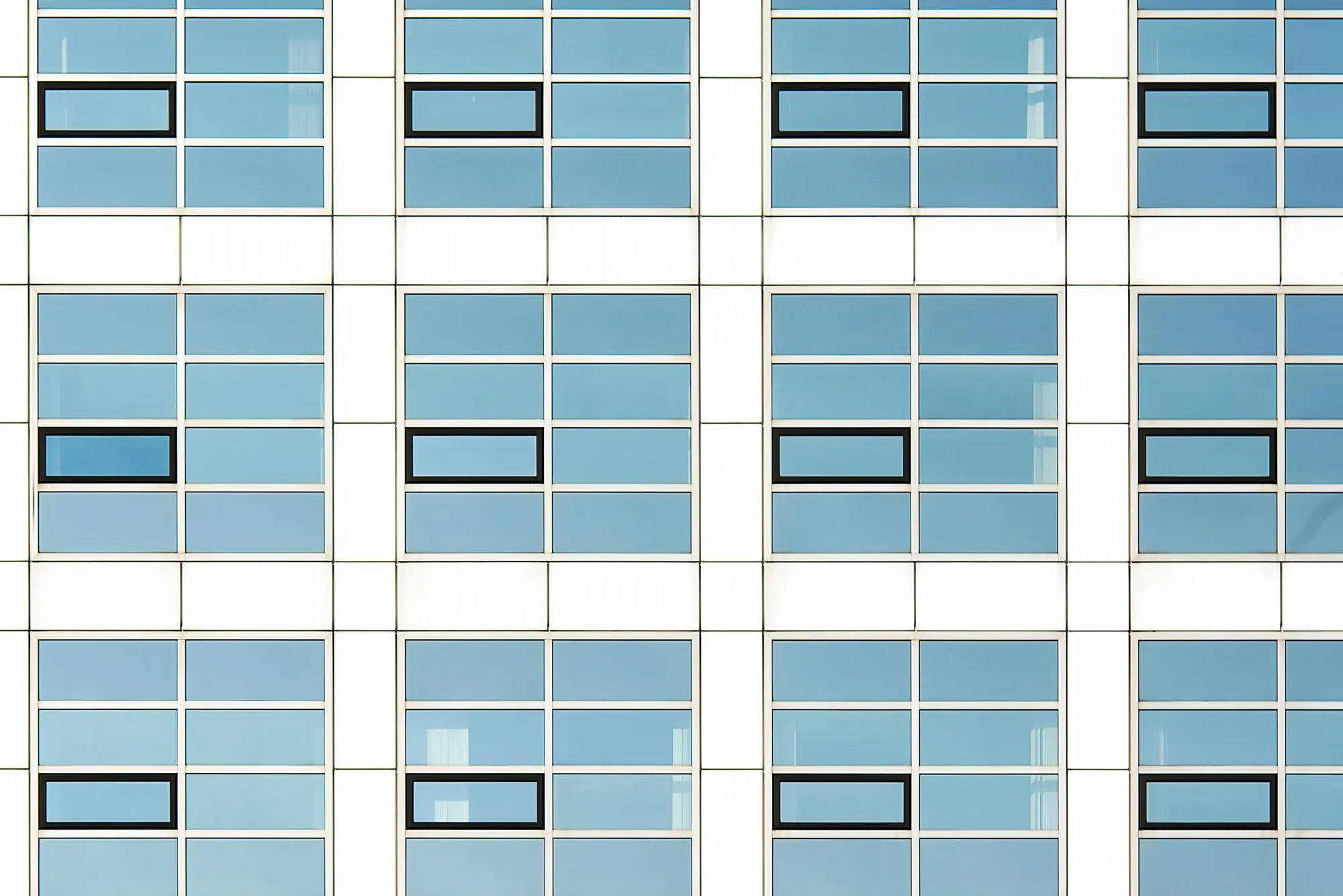 A repeating grid of windows across a building facade, a few panes picked out in black against the rest.
