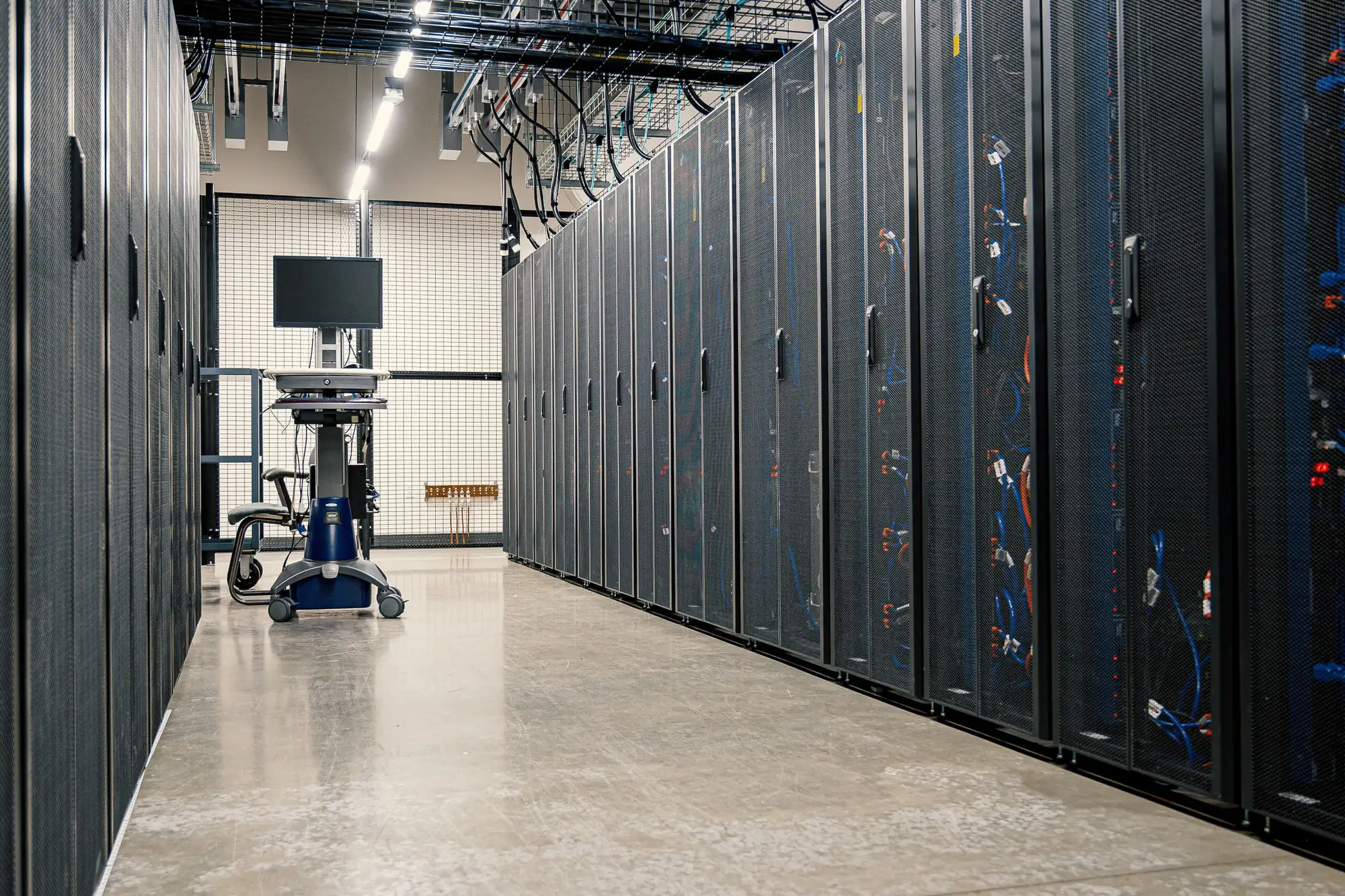 An aisle between rows of server cabinets in a data centre, cabling visible along one side.
